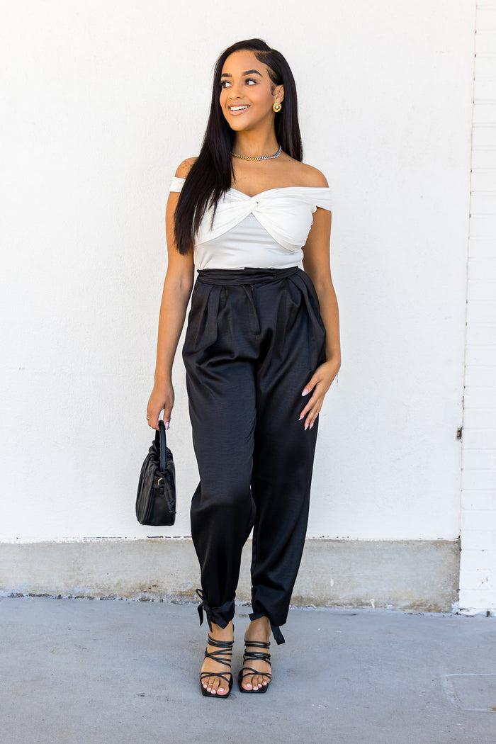 White off-the-shoulder top with twisted front detail and short sleeves, worn with navy trousers.