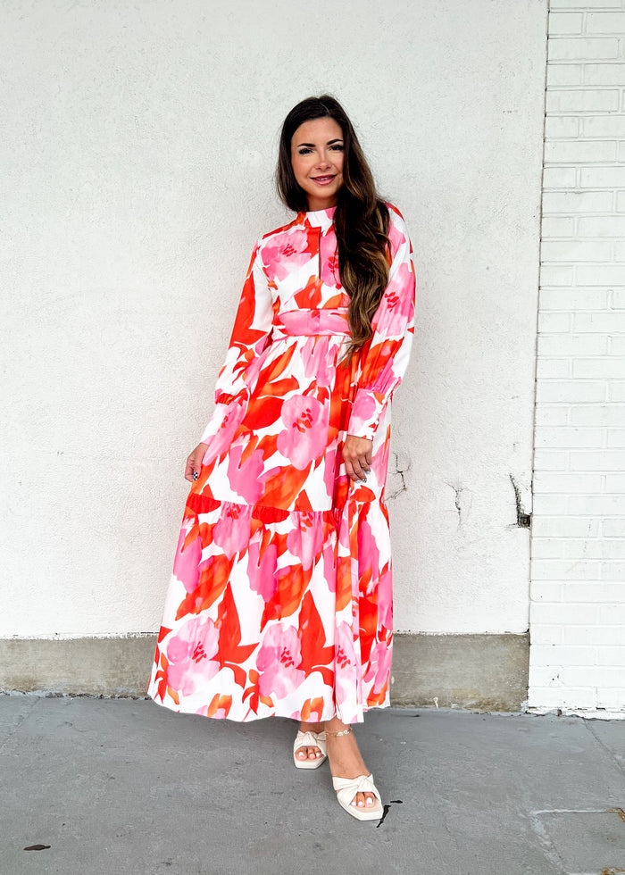 Woman wearing a red and pink floral maxi dress with long sleeves and a tiered skirt.