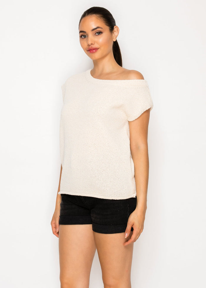 Cream textured short-sleeve top with one-shoulder neckline and side slit, paired with black shorts.