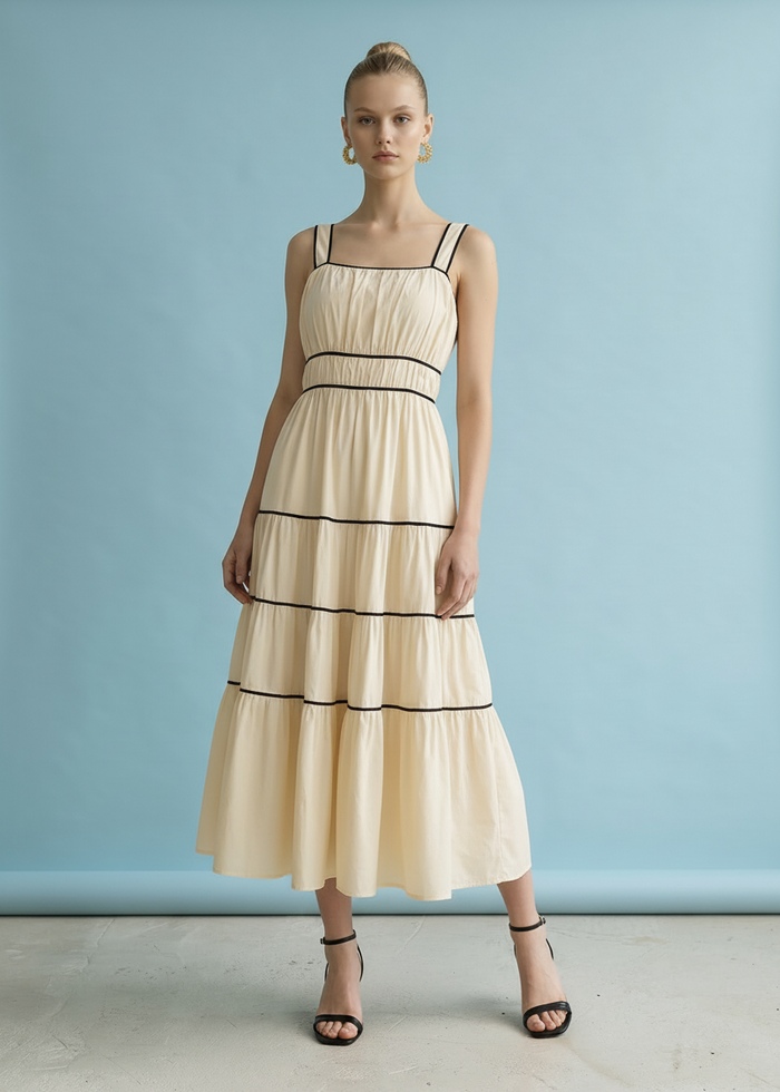 Cream midi dress with black contrast trim bands and tiered layers, thin straps, worn with black heeled sandals.
