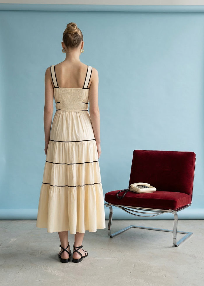 Cream tiered midi dress with black trim straps and ruched waist, shown from back view on model.