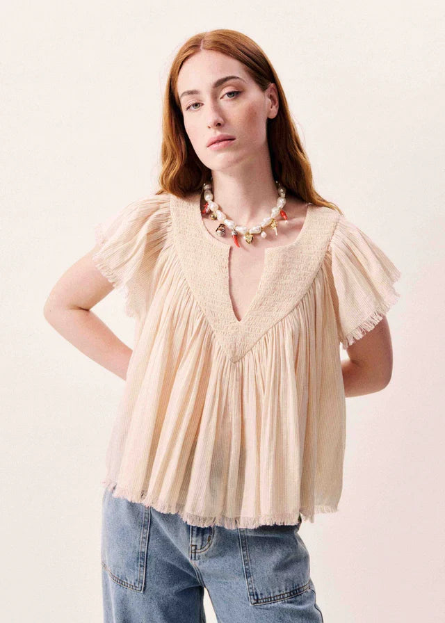 Beige short-sleeve pleated top with V-neckline and ruffled flutter sleeves on model wearing blue jeans.