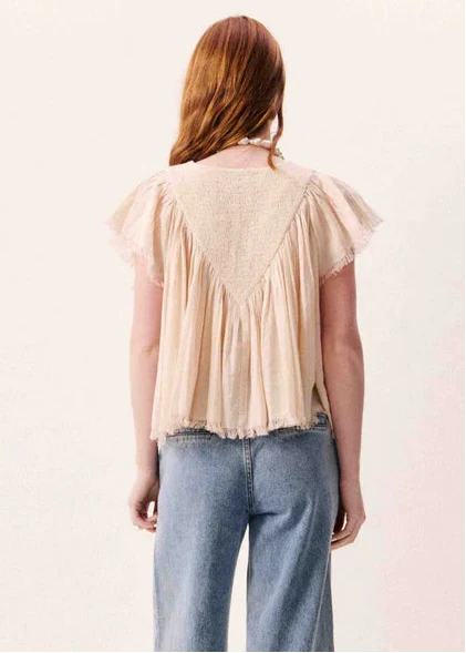 Woman wearing cream short-sleeve top with pleated back panel and ruffled sleeves, paired with blue jeans.