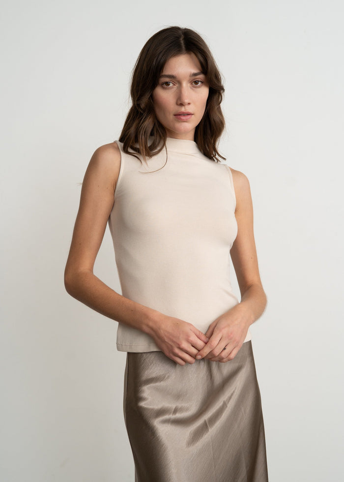 Woman wearing a beige sleeveless top and satin skirt against a plain background