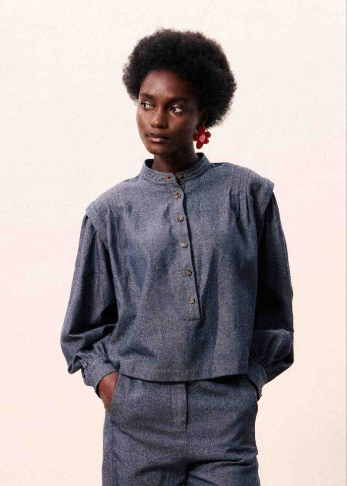 Navy blue chambray shirt with button front and long sleeves, worn with one hand in pocket.