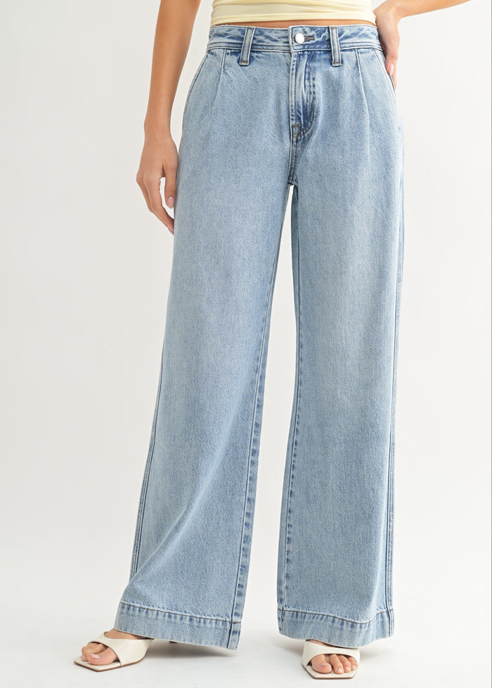 Light-wash relaxed jeans with wide legs and draped fabric through the hips and thighs.