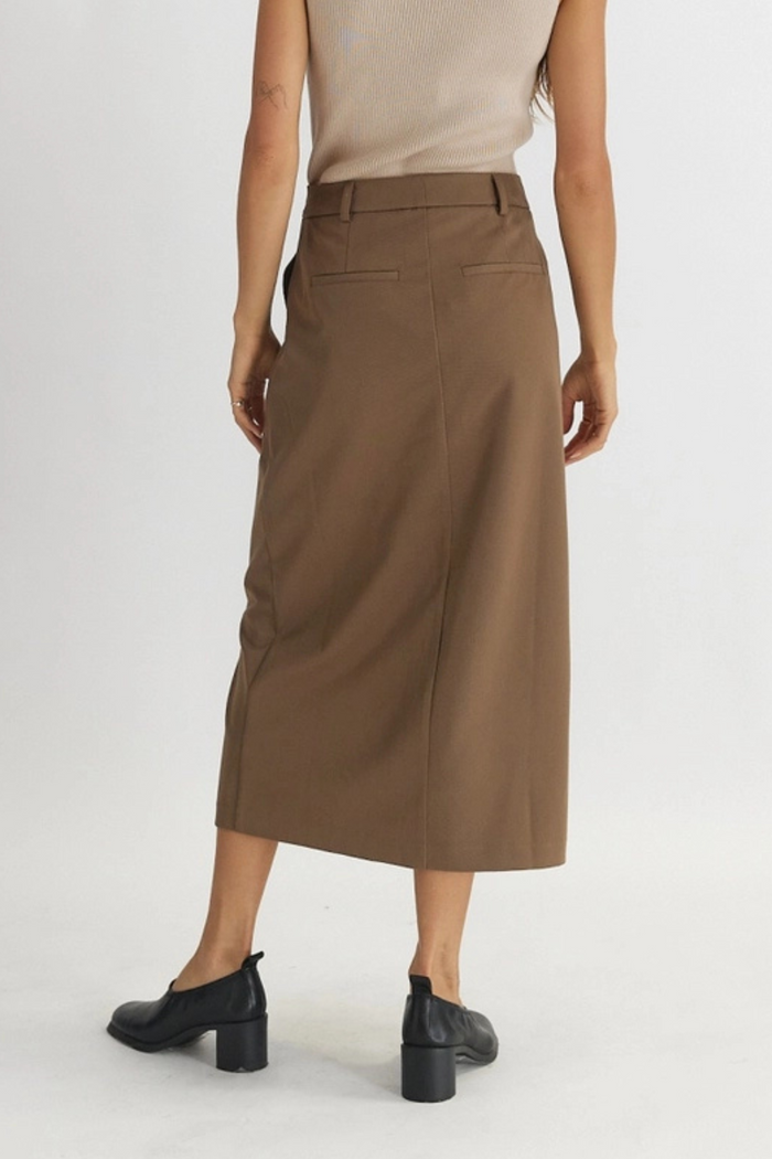 Brown tailored midi skirt with back patch pockets, worn with beige sleeveless top and black heeled boots.