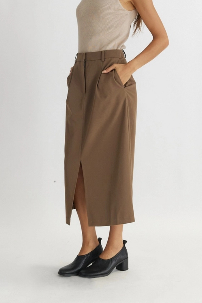 Taupe midi skirt with front slit, high waistband, and side pockets worn with black ankle boots.