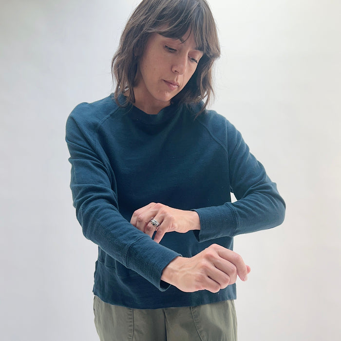 Raglan Sweatshirt in Ink — three-quarter front view, model rolling up sleeve to show ribbed cuff detail, styled with olive trousers