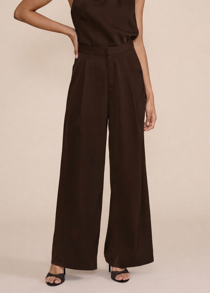 Brown satin wide-leg pants with pleated waistband and high rise, worn with black slide sandals.