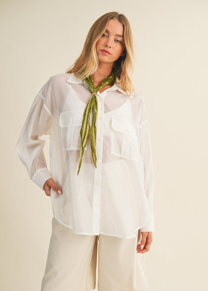 White button-down shirt with collar and chest pockets, worn with a green patterned neck scarf.