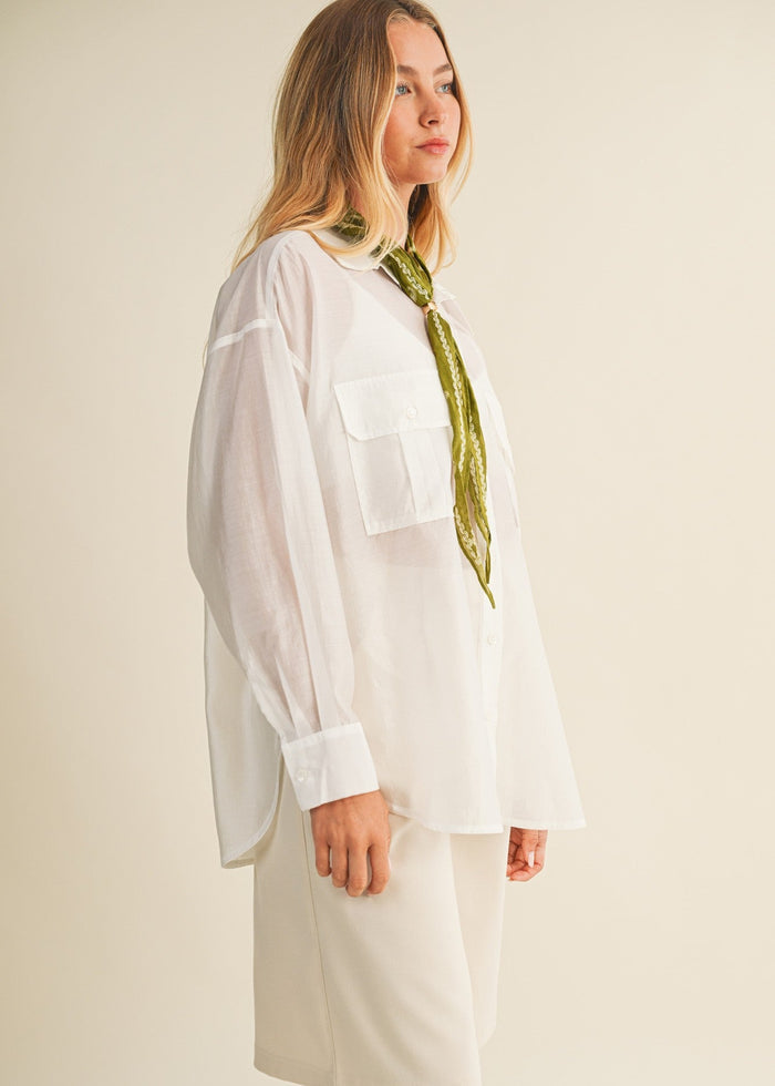 White button-down shirt with chest pockets and rolled sleeves, styled with a green scarf.