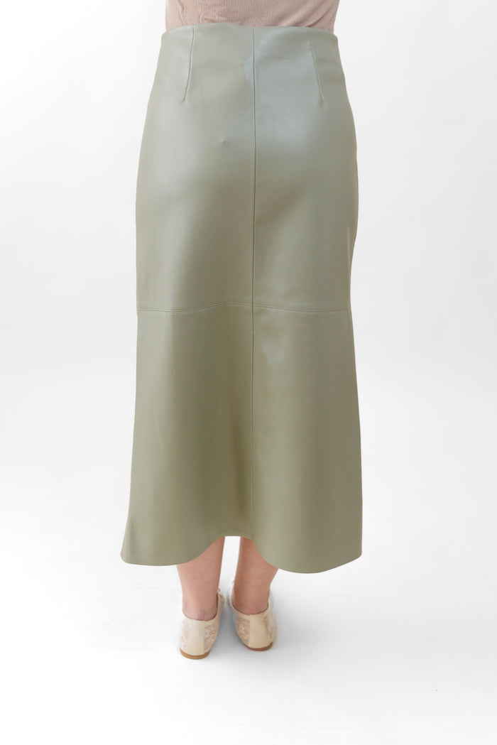 Sage green faux leather midi skirt with center seam detail, shown from back on model wearing cream platform shoes.