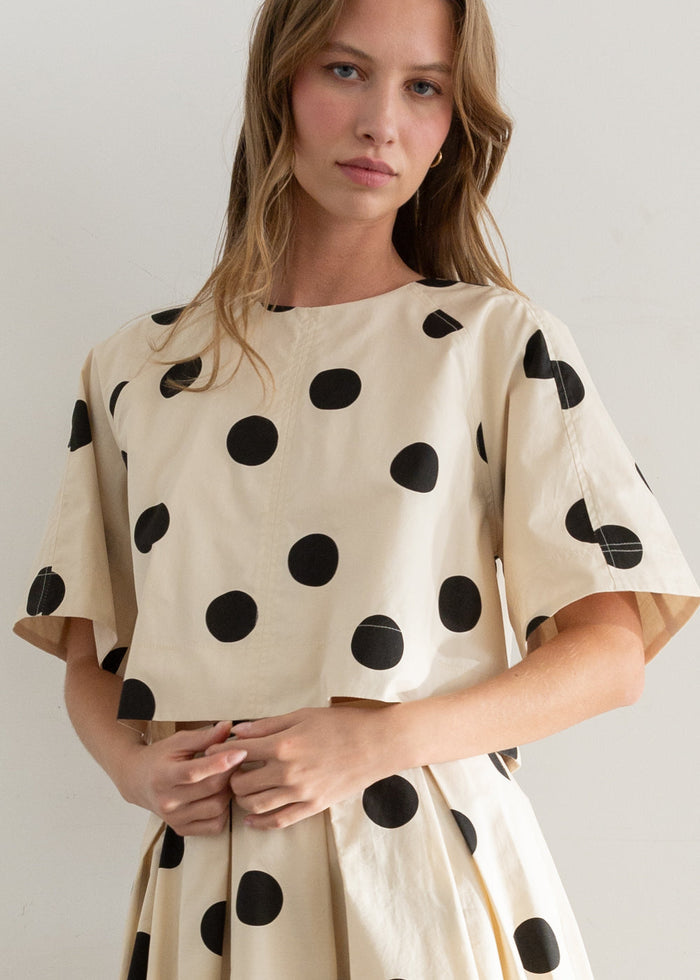Cream short-sleeve top with black polka dots throughout, crew neckline, relaxed fit.
