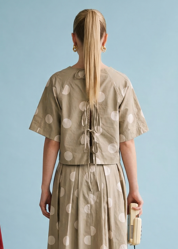 Beige short-sleeve top with white polka dots and back tie detail, shown from rear view.