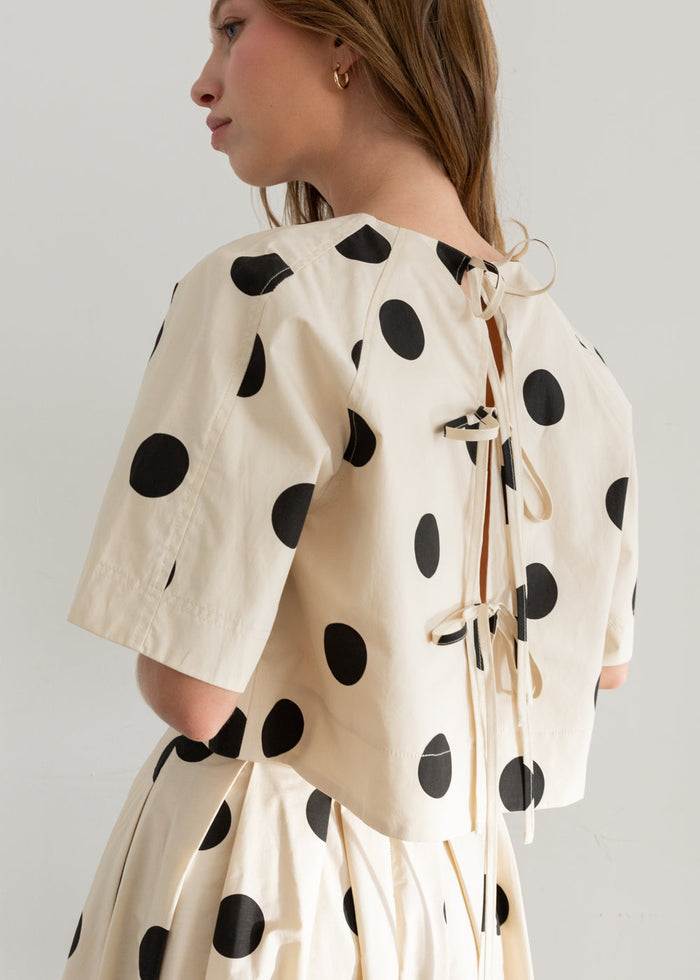 Cream-colored top with black polka dots and back lace-up closure.