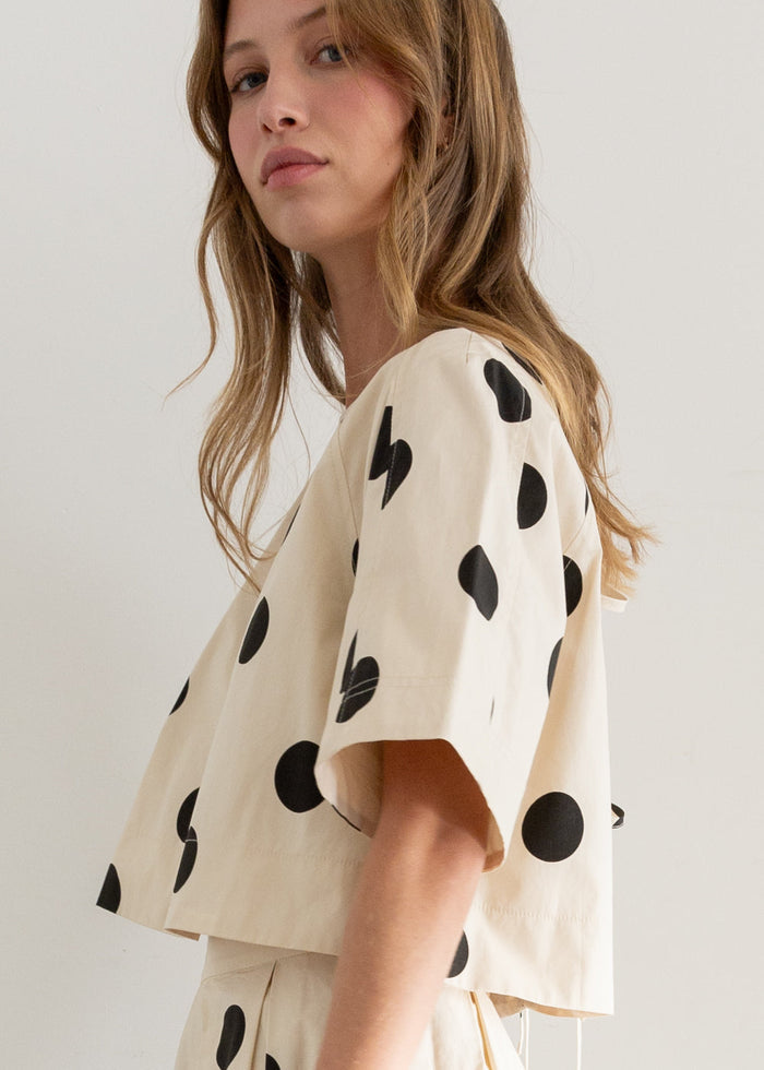 Cream short-sleeve top with black polka dot pattern, worn by model shown from side angle.