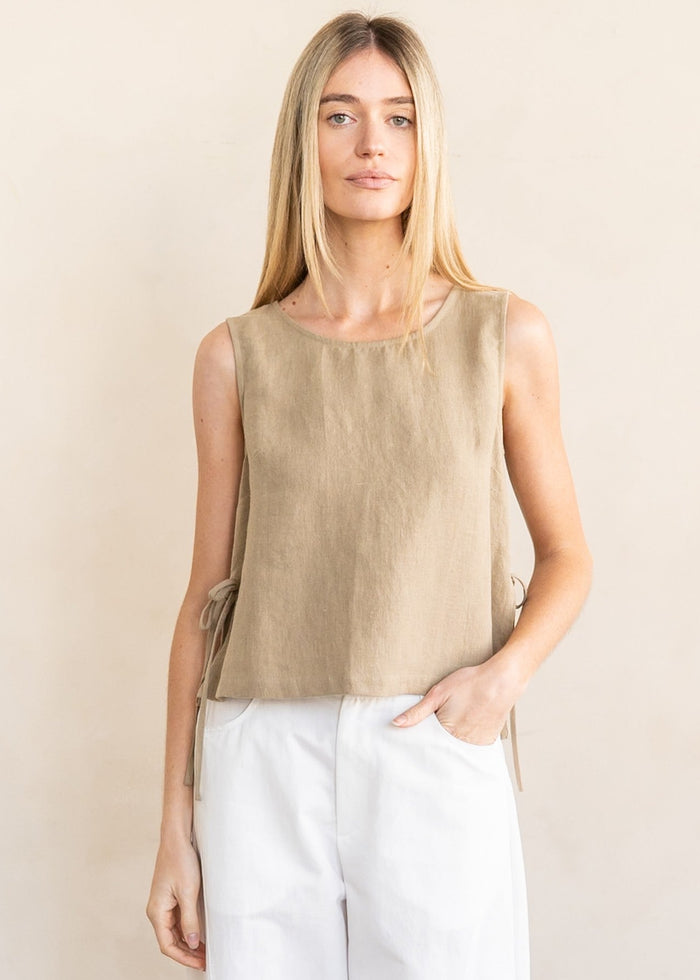 Beige sleeveless linen top with round neckline and side ties, styled with white pants.