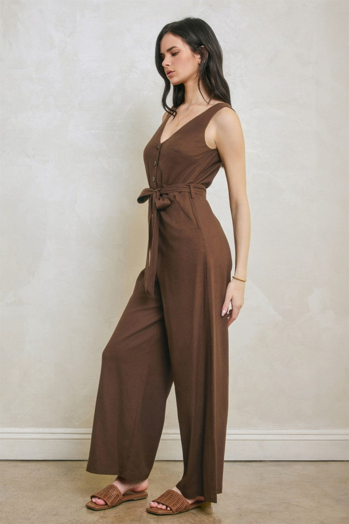 Brown sleeveless jumpsuit with V-neckline, button front, and tied waist belt worn by model.
