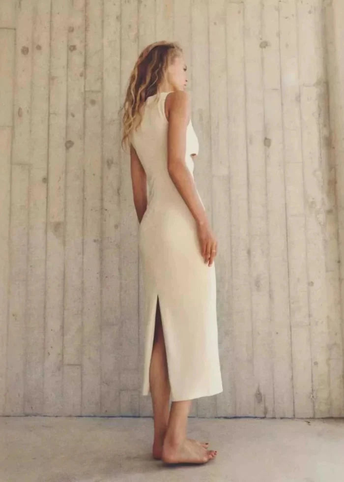 Cream sleeveless maxi dress with open back cutout and front slit, shown on model in profile view.
