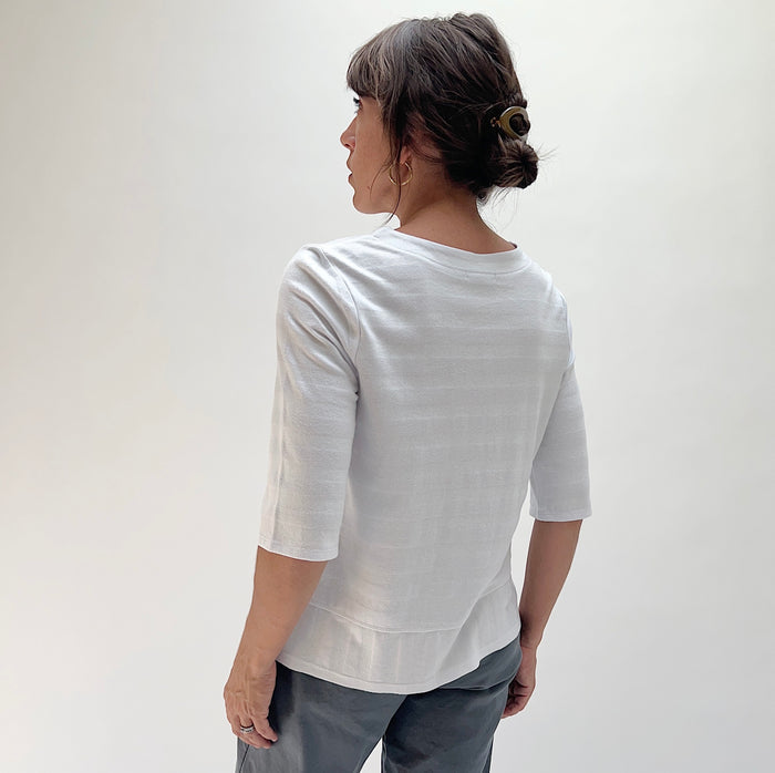 Back view of model wearing Habitat white shadow stripe elbow sleeve top, showing relaxed fit, elbow-length sleeves, and curved layered hem