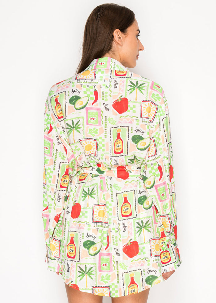 Woman wearing long-sleeve top with multicolored food and spice print including avocados, peppers, tomatoes, and sauce bottles