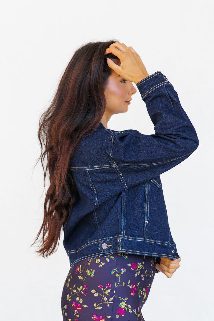 Dark blue denim jacket with contrast stitching, shown from the side on a model wearing floral pants.