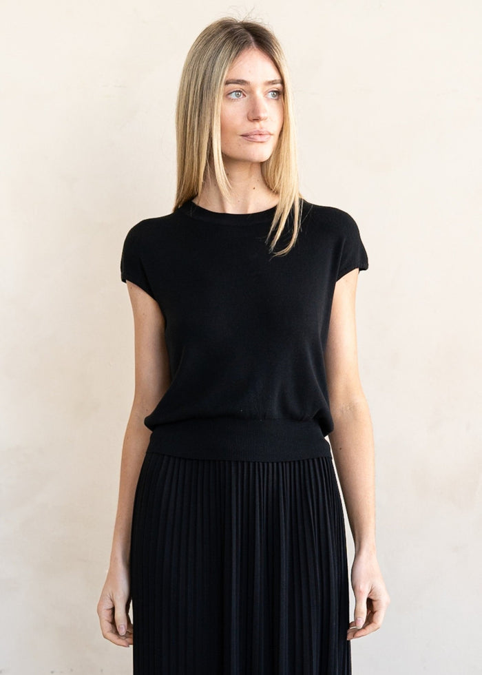 Black short-sleeve knit top with crew neckline and ribbed waistband, worn with pleated skirt.
