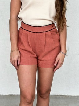 Rust-colored textured shorts with pleated front and elastic waistband, paired with cream short-sleeve top.