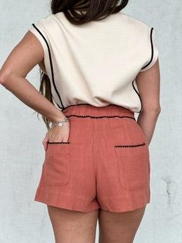 Coral textured pleated shorts with front pockets, paired with cream sleeveless top.