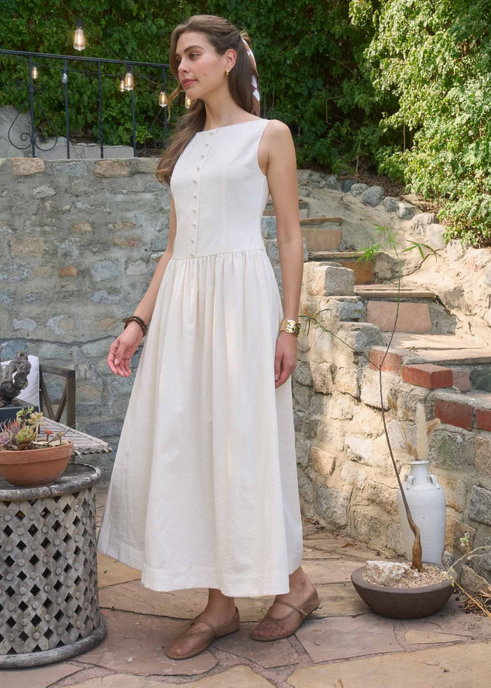 Woman wearing a cream sleeveless midi dress with button front and gathered skirt, paired with brown sandals.