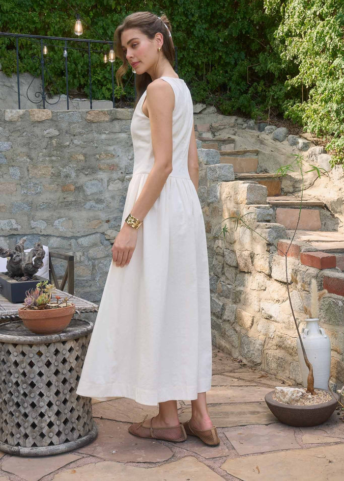 White sleeveless midi dress with fitted bodice and full skirt, worn with woven flat sandals.
