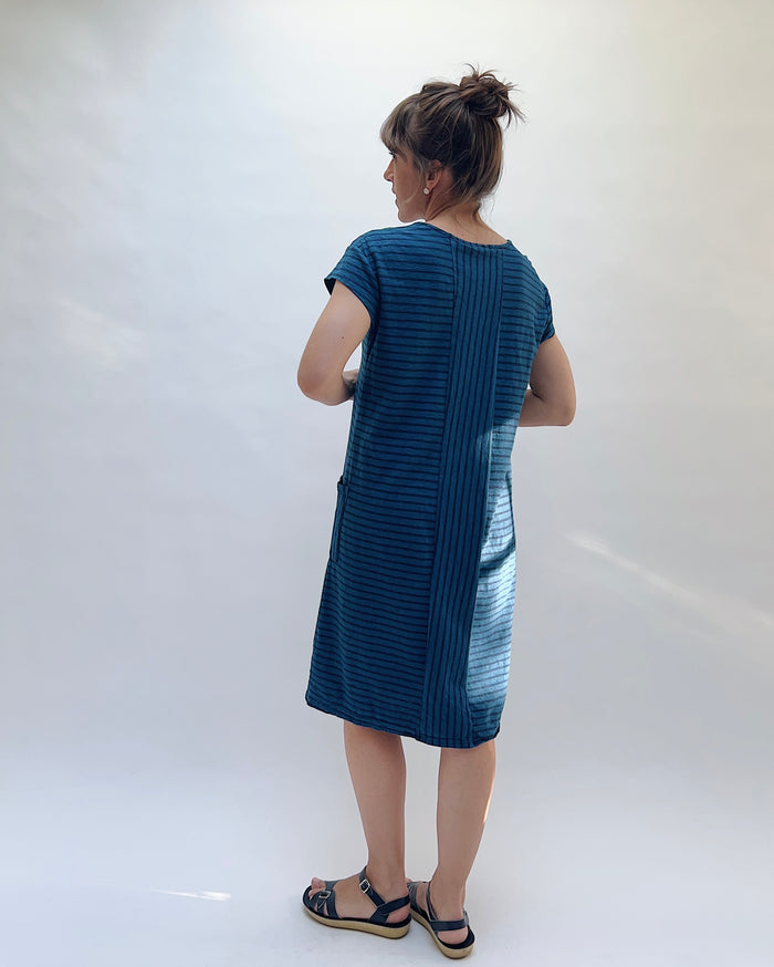 Woman wearing a blue dress with a white background viewed from behind