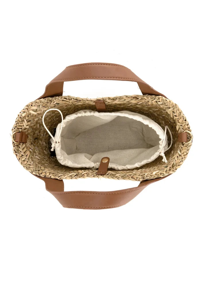 Woven straw tote bag with tan leather handles and cream linen interior lining, viewed from above.