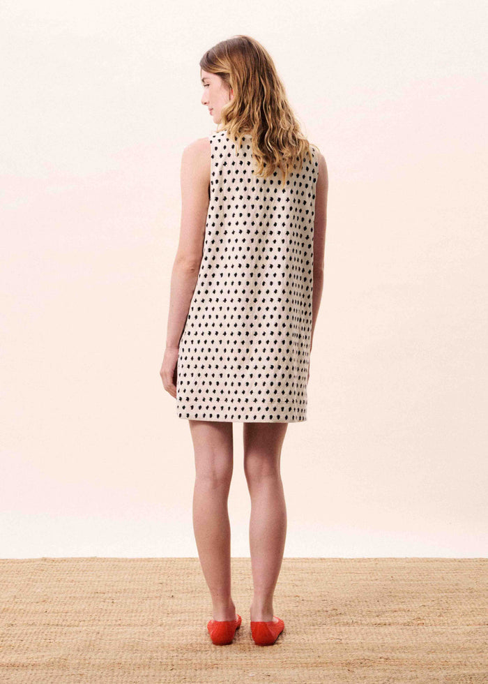 Cream sleeveless shift dress with black diamond pattern, shown from back on model wearing red shoes.