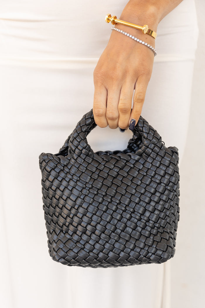 Black woven leather handbag with braided handles held in hand.