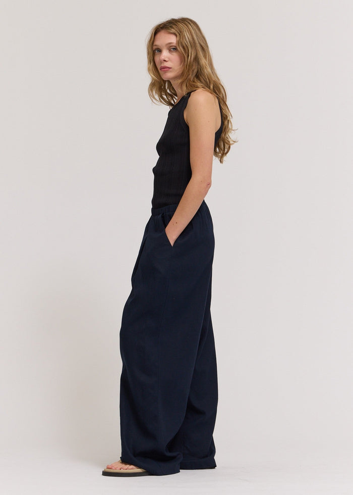 Woman wearing a black sleeveless top and wide-leg pants on a white background