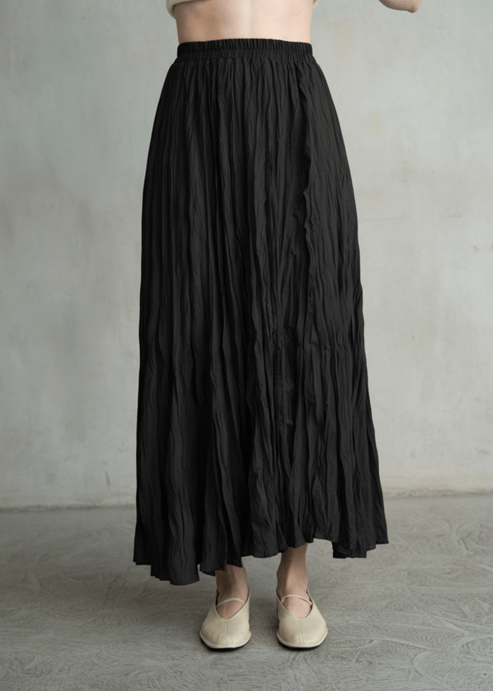 Black crinkled maxi skirt with elasticated waist, featuring vertical texture and a full A-line silhouette.