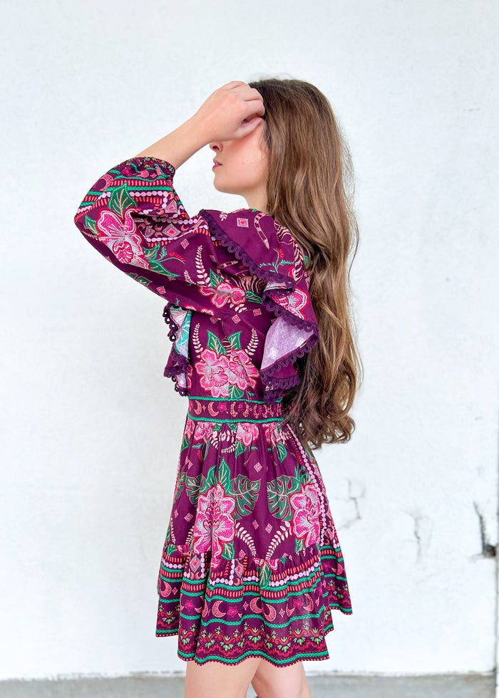 Purple mini dress with pink and green floral embroidered pattern, long ruffled sleeves, and decorative lace trim at hem.
