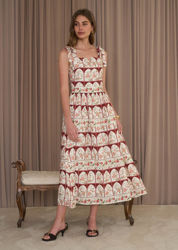 Woman wearing a patterned dress standing in front of a curtain with a bench.