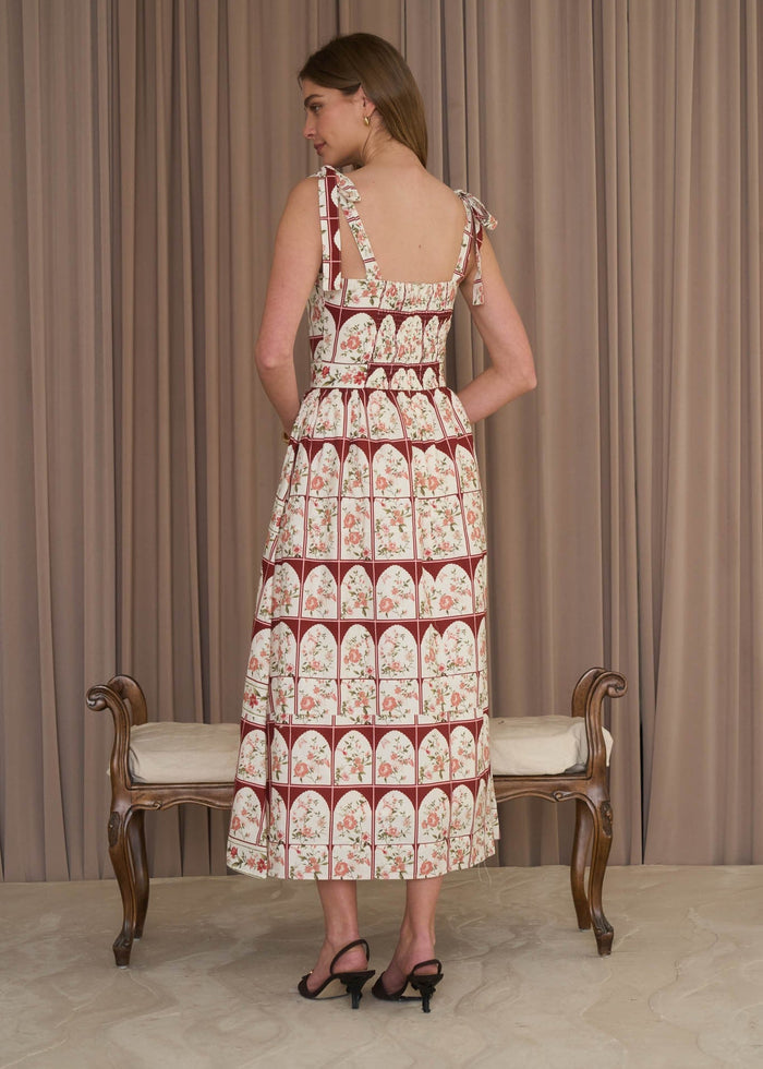 Woman wearing a patterned dress standing in front of a beige curtain.