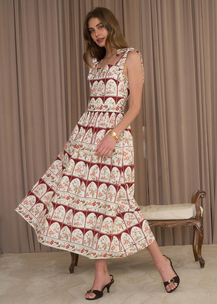 Woman wearing a patterned dress standing in front of a beige curtain.