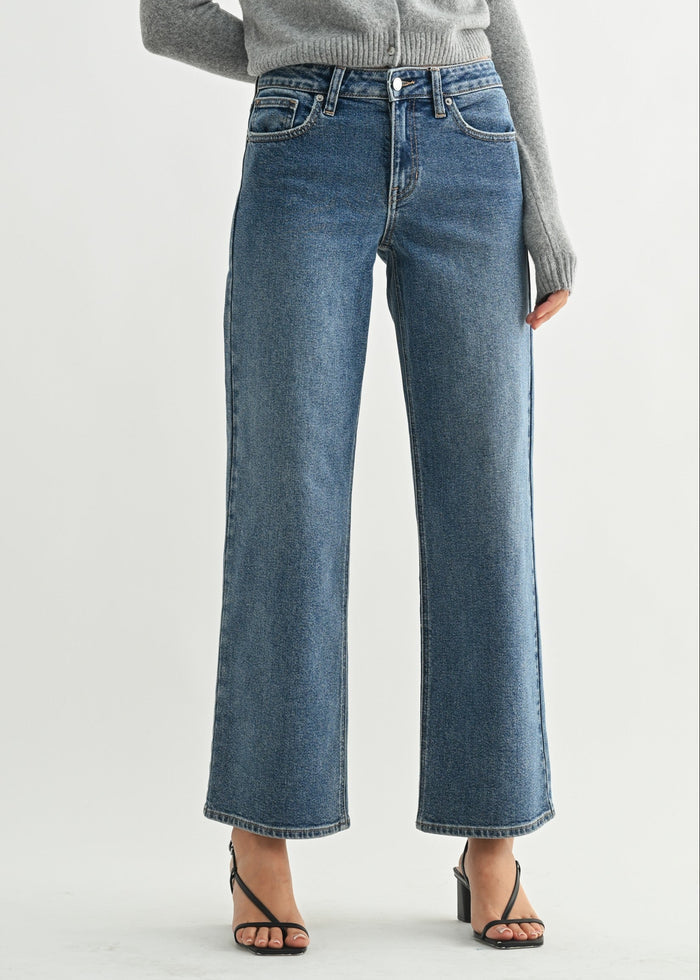 Medium-wash mid-rise jeans with straight legs and white stitching details, worn with a gray cardigan and black sandals.