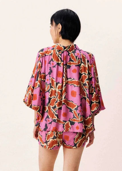 Woman wearing a pink floral puff sleeve top with orange and purple leaf pattern, shown from back view.