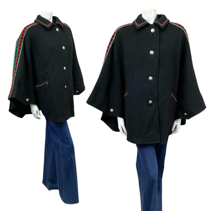 Vintage 60s 70s black collared cape with red and green folk embroidery on a white mannequin wearing blue flared jeans