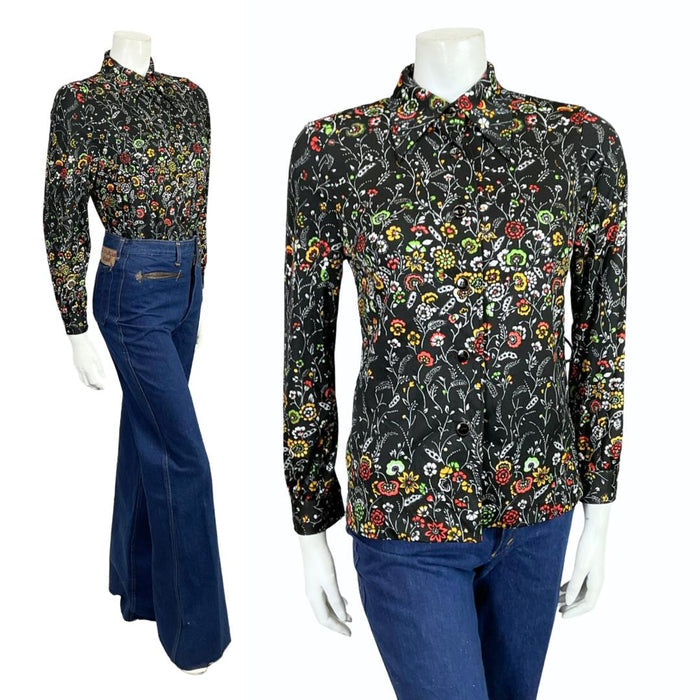 Mannequin wears a black white green and red floral printed 60s 70s dagger collar shirt with blue flared jeans.