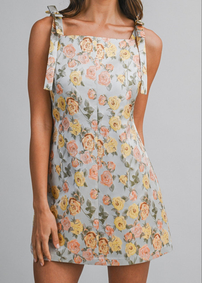 Light blue mini dress with pink, yellow, and coral floral pattern and tied shoulder straps.