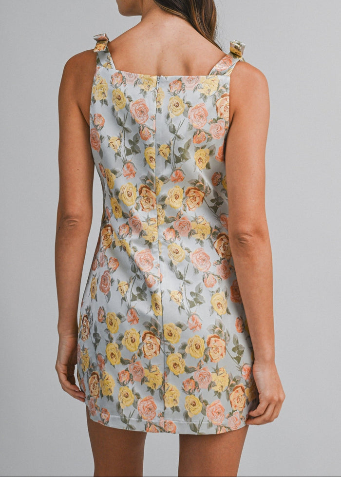 Light blue mini dress with yellow, pink, and coral rose print and tied shoulder straps, shown from back view.